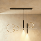 Clérachic mirrored layout pendant with two gold rings left, a ring right and two black spot cylinders on a limewash wall.