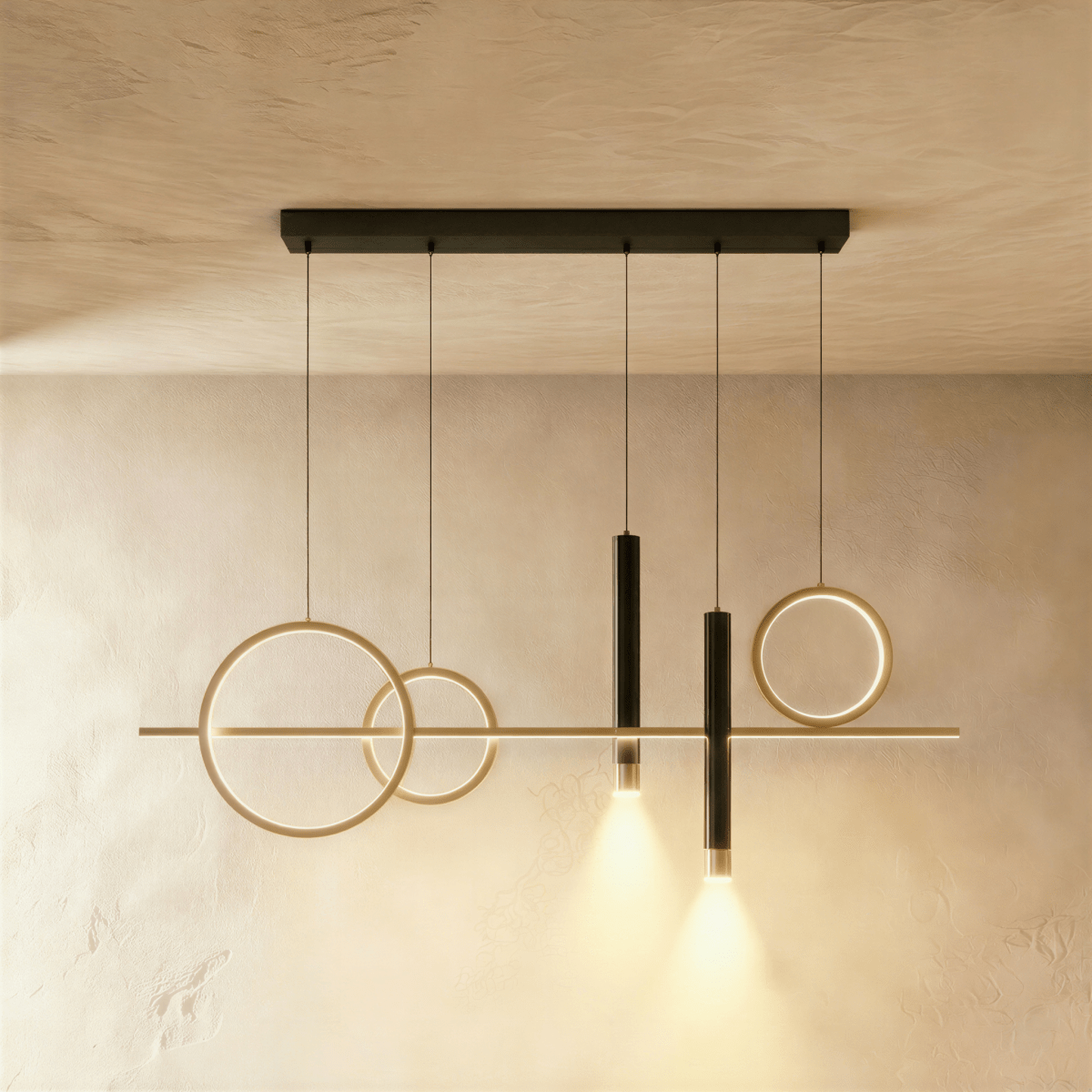 Clérachic gold pendant light with three gold rings, a slim bar and two black spot cylinders glowing warmly on limewash.