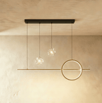 Clérachic gold pendant light with a shorter bar, one ring and two clear sparkling glass globes on a limewash wall.