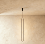 Clérachic slim black stadium-shaped LED loop pendant hanging long from a small black canopy against limewash.