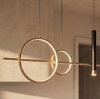 Close view of the Clérachic gold pendant light, two glowing rings crossing a slim bar beside a black spot cylinder.