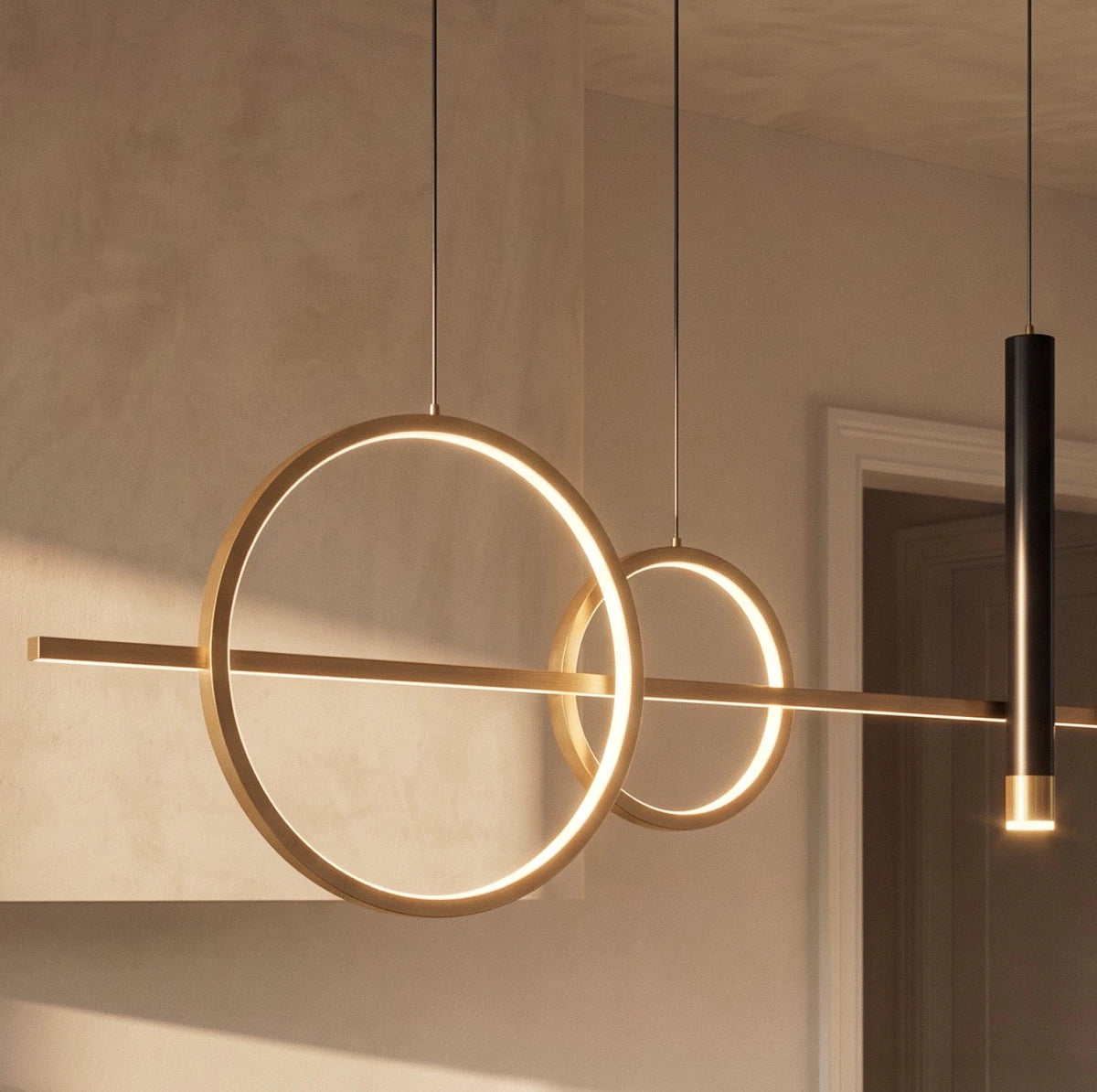 Close view of the Clérachic gold pendant light, two glowing rings crossing a slim bar beside a black spot cylinder.
