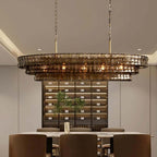A Clérachic linear chandelier in smoky brown glass tiers glowing above a marble dining table in front of a lit wine wall.