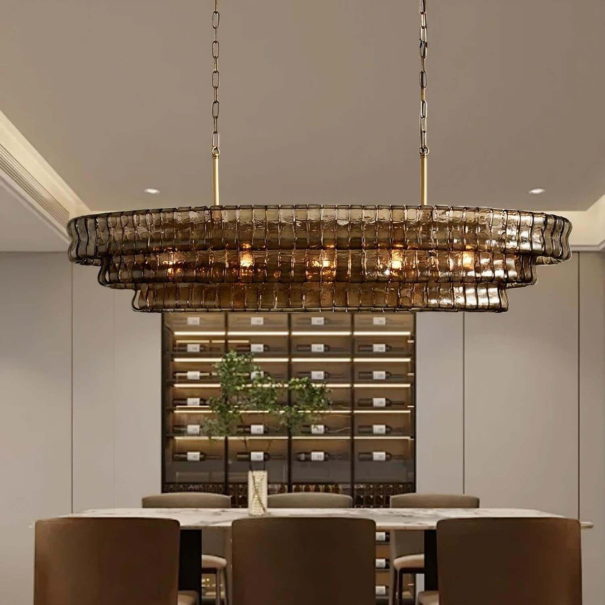 A Clérachic linear chandelier in smoky brown glass tiers glowing above a marble dining table in front of a lit wine wall.