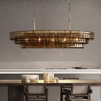 Smoke-brown stepped glass tiers of this Clérachic chandelier, lit warm, hanging above a dark wood table by a pale kitchen counter.