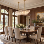 Clear glass tiers on this Clérachic chandelier hang with brass-coloured stems in a panelled dining room with a carved wooden table.