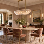 Clear glass tiers of this Clérachic chandelier light a blush-pink dining room with an oval stone table and dusty-rose chairs.