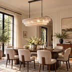 Hanging low over a dark wood table with cream chairs, this Clérachic chandelier shows clear rippled glass and a black canopy.