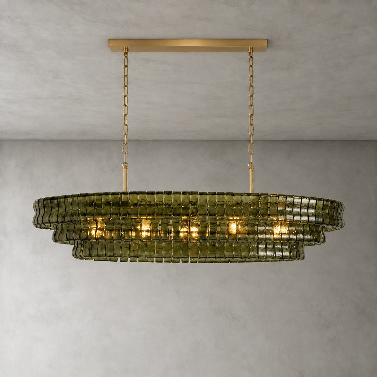 Green glass tiers on this Clérachic chandelier, shown with a gold long canopy bar against a soft grey concrete-look wall.