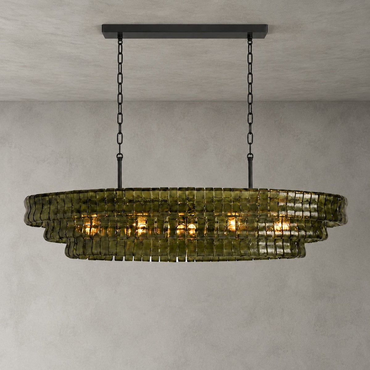 This Clérachic chandelier in green glass hangs from a black long canopy on black chains, lit, on a plain grey backdrop.