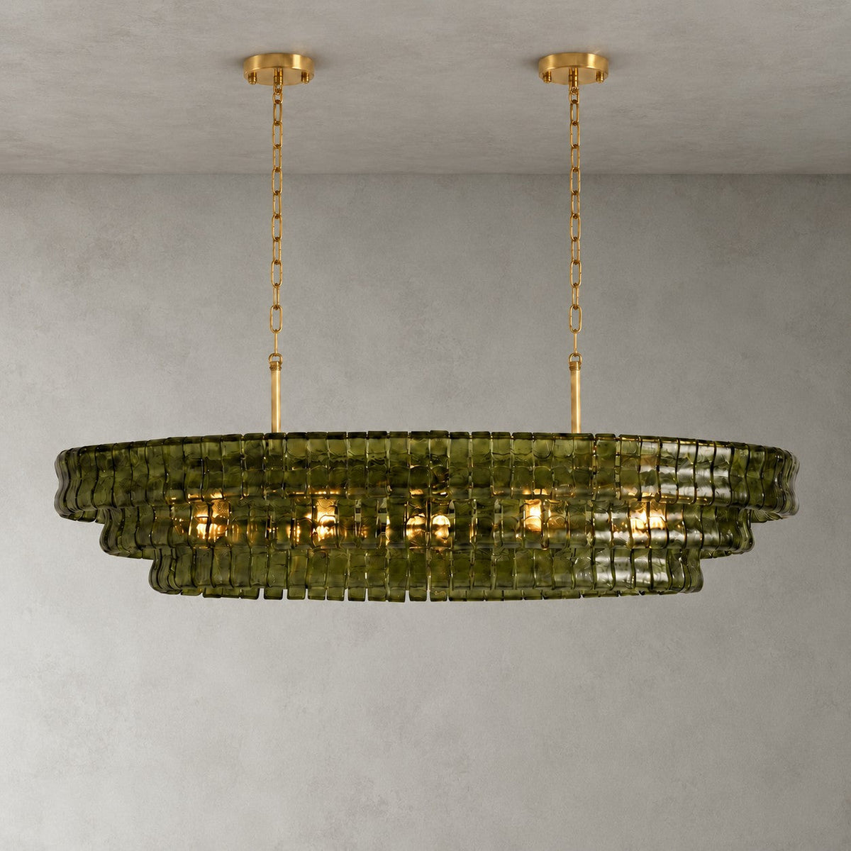 A green-glass Clérachic chandelier with two gold round canopies and slim stems, lit against a grey wall.
