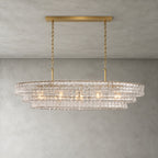 Clear glass tiers of this Clérachic chandelier, held by a gold long canopy bar and chains, lit on a grey wall.