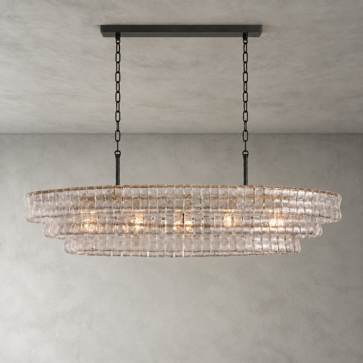 A clear-glass Clérachic chandelier with a black long canopy and black chains, glowing softly on a grey backdrop.