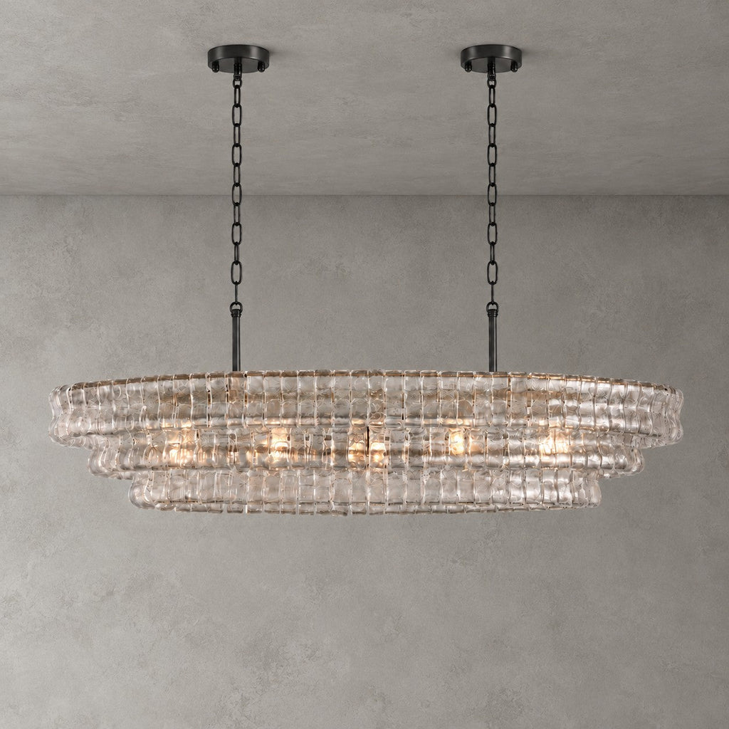 Clear glass tiers on a Clérachic chandelier with two black round canopies, lit against a grey concrete-look wall.