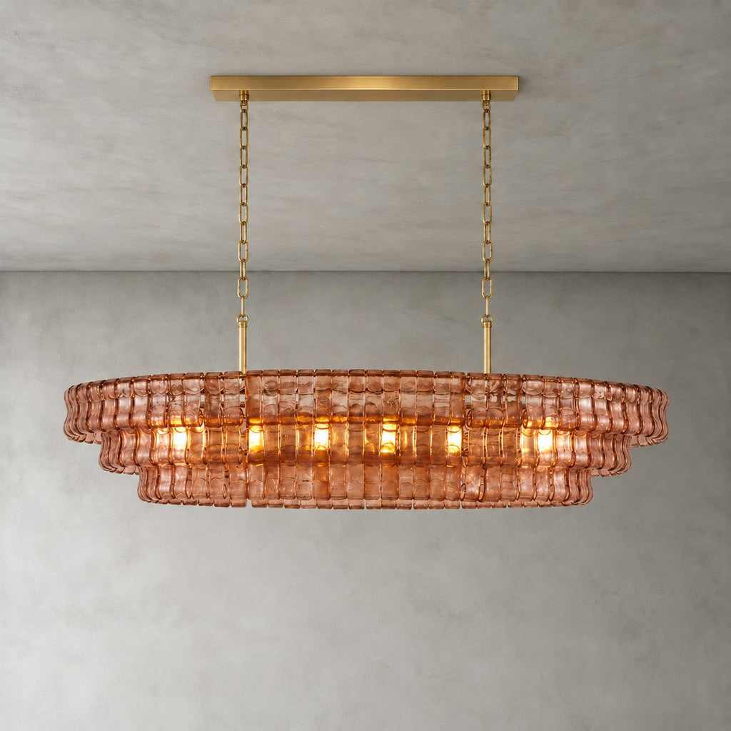 A rose-pink Clérachic chandelier with a gold long canopy bar, its warm bulbs glowing through the glass tiers.