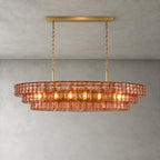 A rose-pink Clérachic chandelier with a gold long canopy bar, its warm bulbs glowing through the glass tiers.