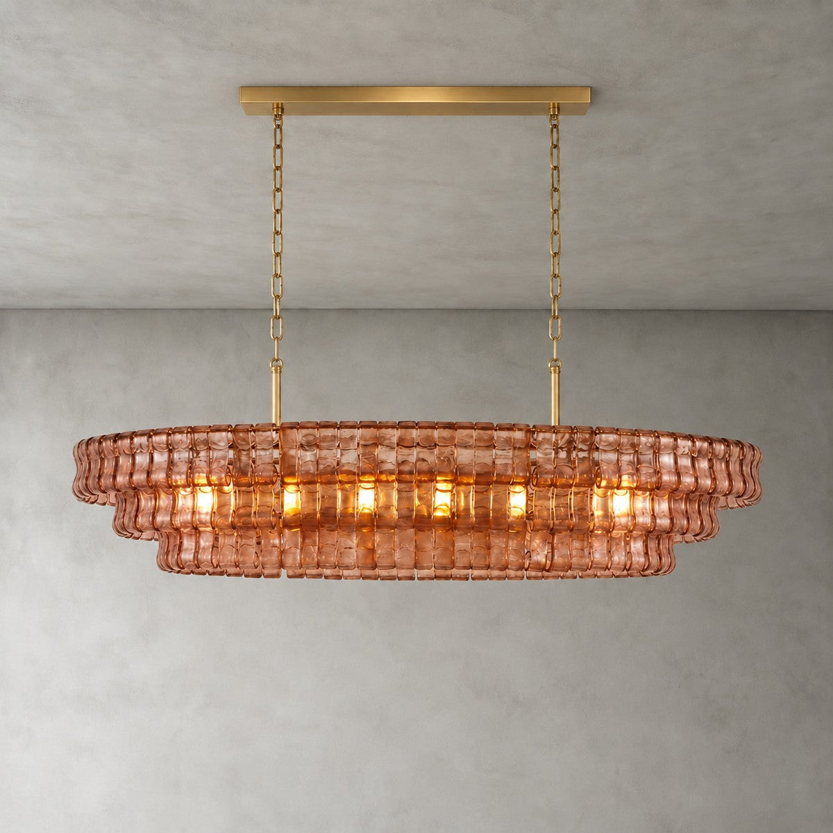 A rose-pink Clérachic chandelier with a gold long canopy bar, its warm bulbs glowing through the glass tiers.