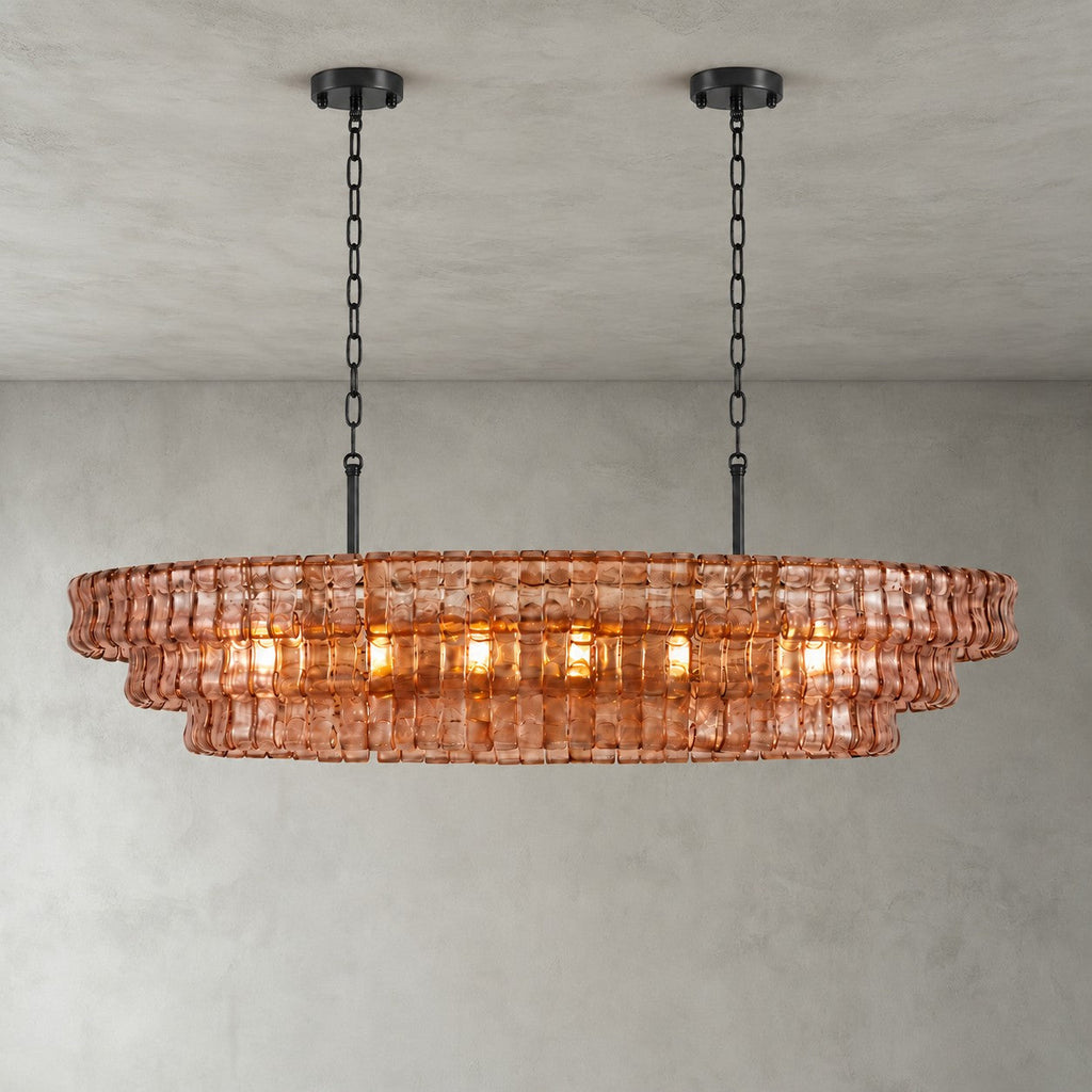 A pink-glass Clérachic chandelier with two black round canopies and black chains, its bulbs glowing on a grey backdrop.