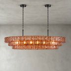 A pink-glass Clérachic chandelier with two black round canopies and black chains, its bulbs glowing on a grey backdrop.
