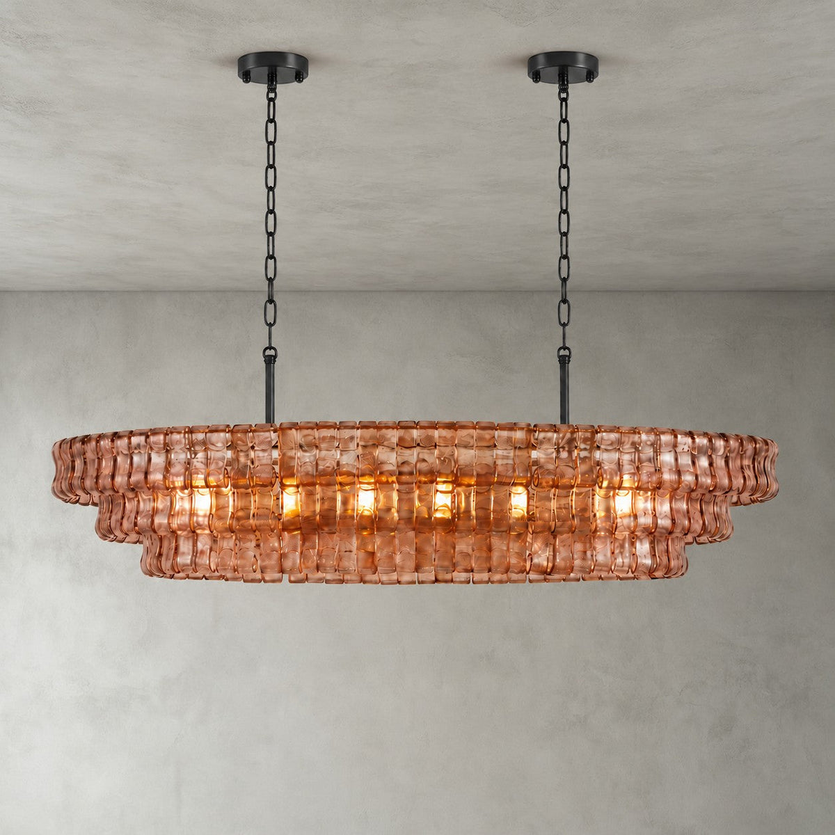 A pink-glass Clérachic chandelier with two black round canopies and black chains, its bulbs glowing on a grey backdrop.