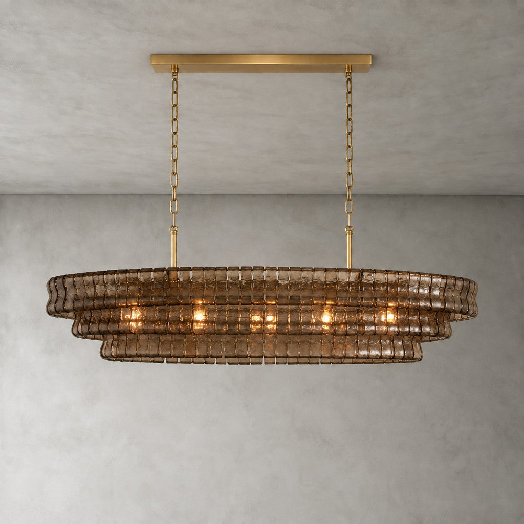 Smoky brown glass tiers on a Clérachic chandelier held by a gold long canopy bar, shown lit against a grey wall.