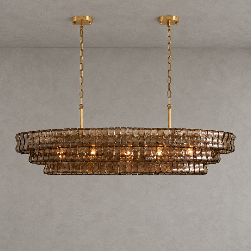 A smoke-brown Clérachic chandelier with two gold round canopies and slim stems, softly lit against a grey wall.