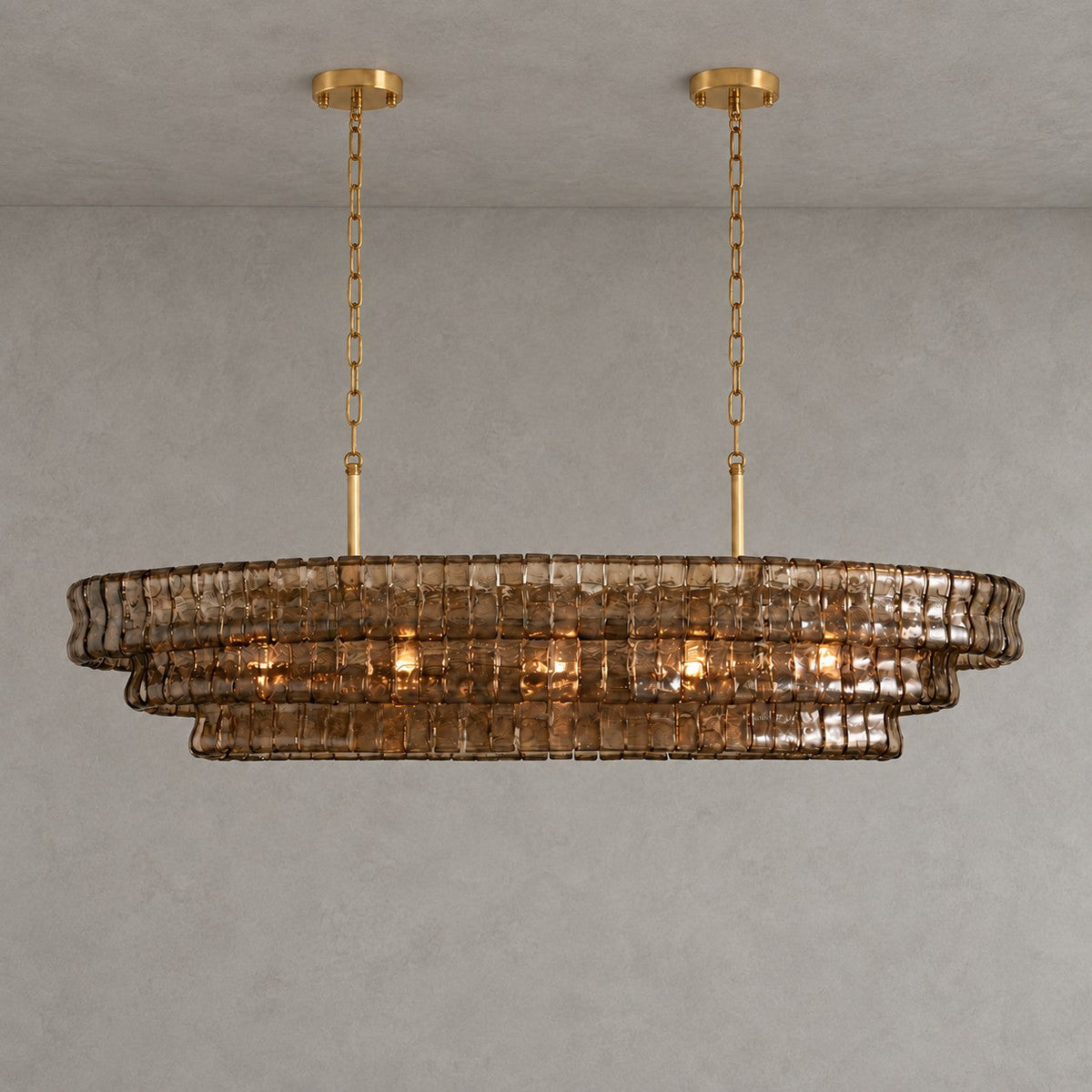 A smoke-brown Clérachic chandelier with two gold round canopies and slim stems, softly lit against a grey wall.
