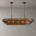 Smoke-grey glass tiers on this Clérachic chandelier with two black round canopies, glowing warm on a concrete-look wall.
