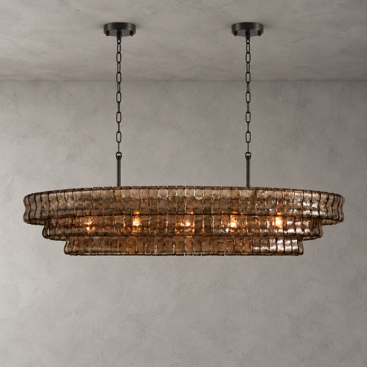 Smoke-grey glass tiers on this Clérachic chandelier with two black round canopies, glowing warm on a concrete-look wall.