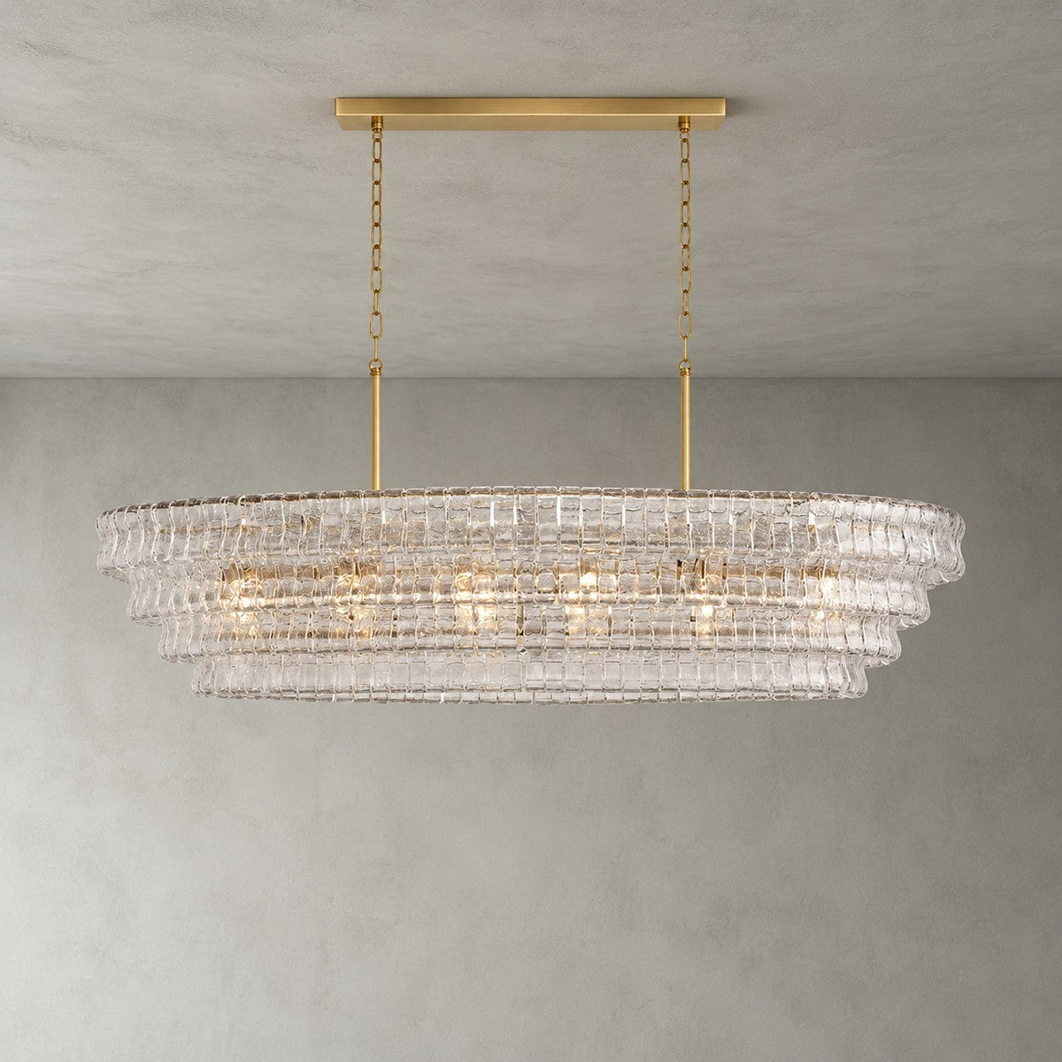 Clear rippled glass on this Clérachic chandelier, with a gold long canopy bar and four stepped tiers, lit on grey.