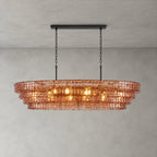 This Clérachic chandelier in rose-pink glass has four stepped tiers and a black long canopy bar, lit on a grey wall.