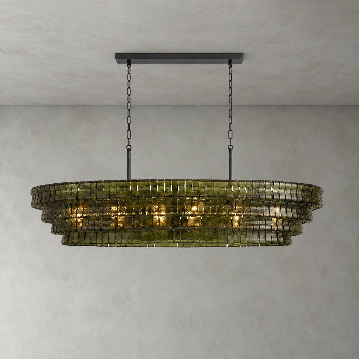 A green-glass Clérachic chandelier with four stepped tiers and a black long canopy bar, glowing on a grey wall.