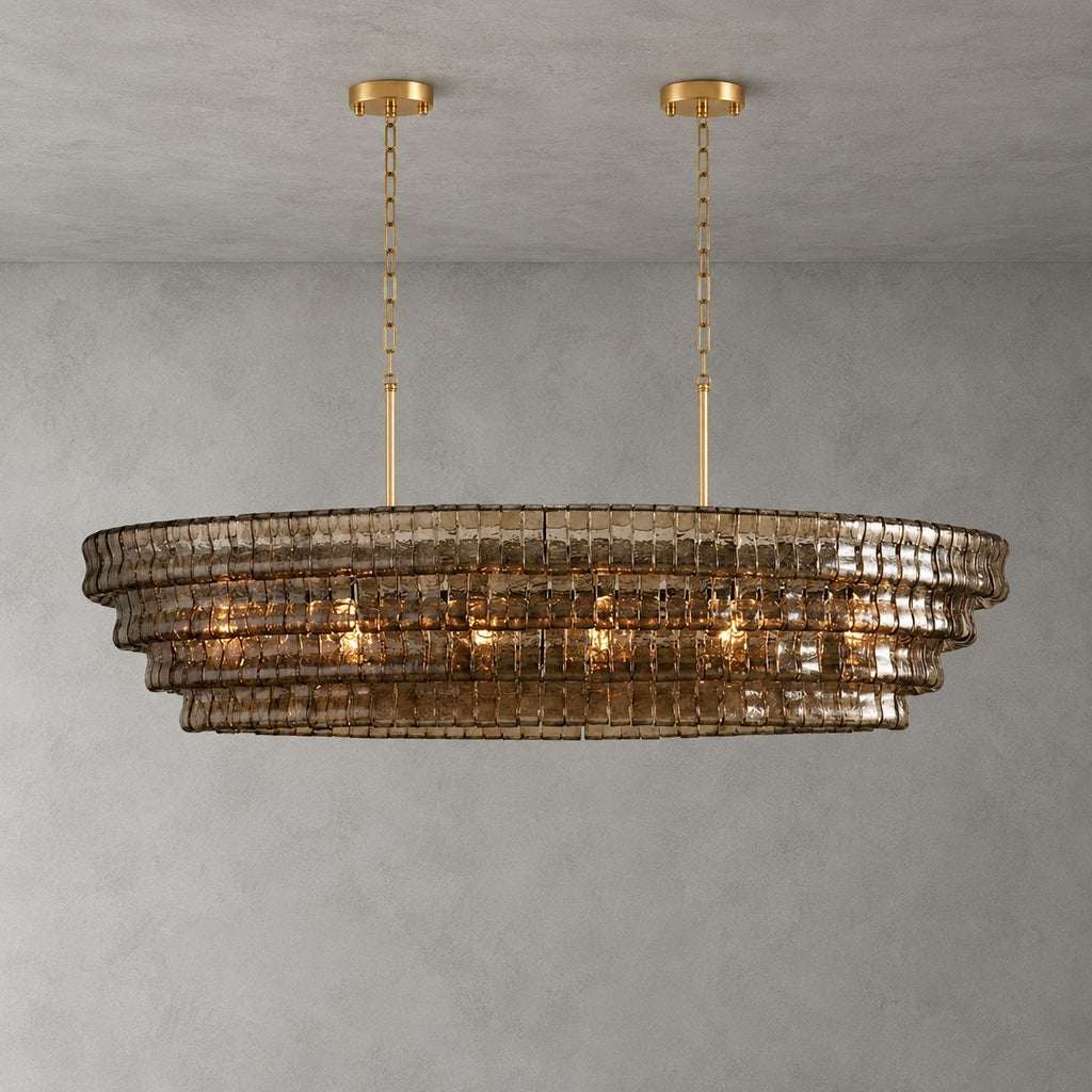 A smoke-brown Clérachic chandelier with four glass tiers, hung from two gold round canopies against a grey backdrop.