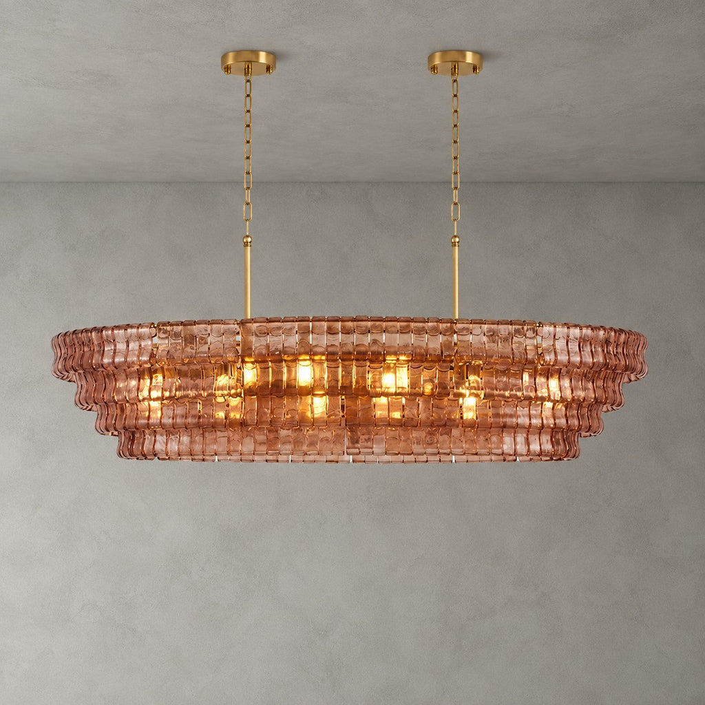 Rose-pink glass tiers of this Clérachic chandelier, with two gold round canopies and chain, lit against grey.