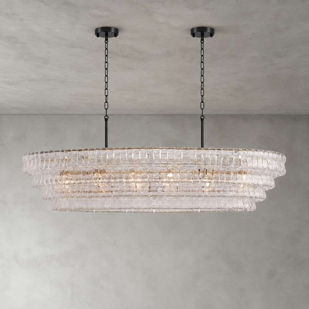 This Clérachic chandelier in pale clear glass, with two black round canopies and four tiers, shown on a grey backdrop.