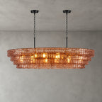 A rose-pink Clérachic chandelier with two black round canopies, its four tiers lit warm against a concrete-look wall.