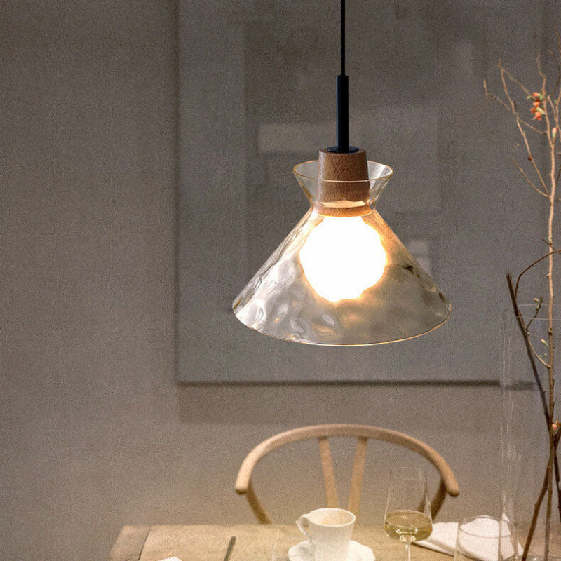 Clérachic cone-shaped pendant light glowing over a dining nook, with a pale wood chair, a coffee cup and a glass of wine below.