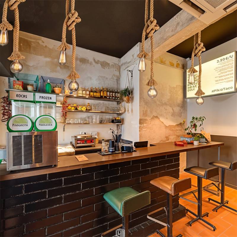 Clérachic hemp rope pendants with filament bulbs hanging over a counter-service bar with a dark brick front and tall stools.