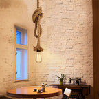 Clérachic single hemp rope pendant with a large knot and a filament bulb, hung in a whitewashed brick room beside a round table.