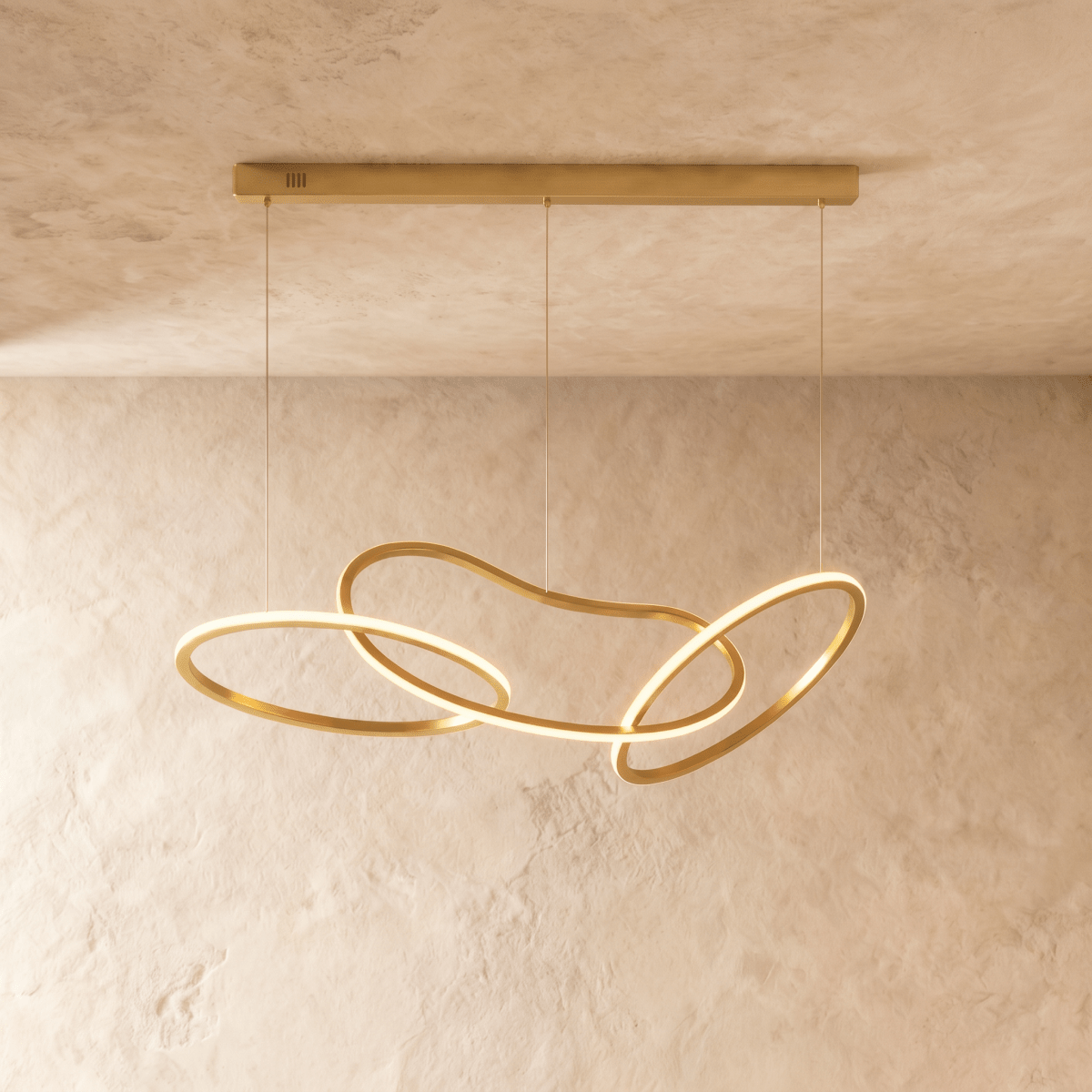 Clérachic chandelier in brushed gold, three interlocking freeform rings glowing warm white beneath a plaster ceiling.