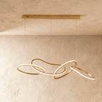 Clérachic chandelier viewed from the side, its sculptural gold loops overlapping in a continuous glowing line.