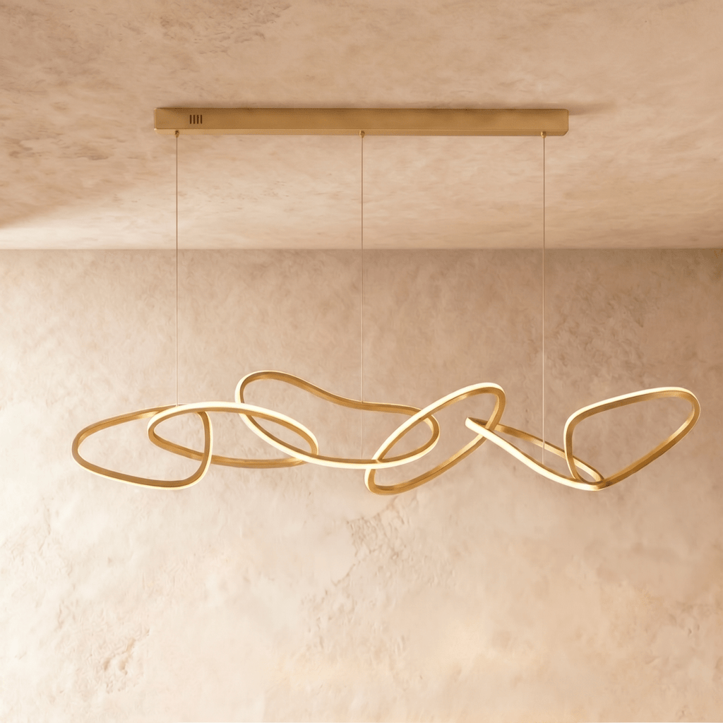 Clérachic chandelier's gold rings cascade in an elongated interlocking chain beneath a textured plaster wall.