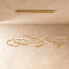 Clérachic chandelier's gold rings cascade in an elongated interlocking chain beneath a textured plaster wall.