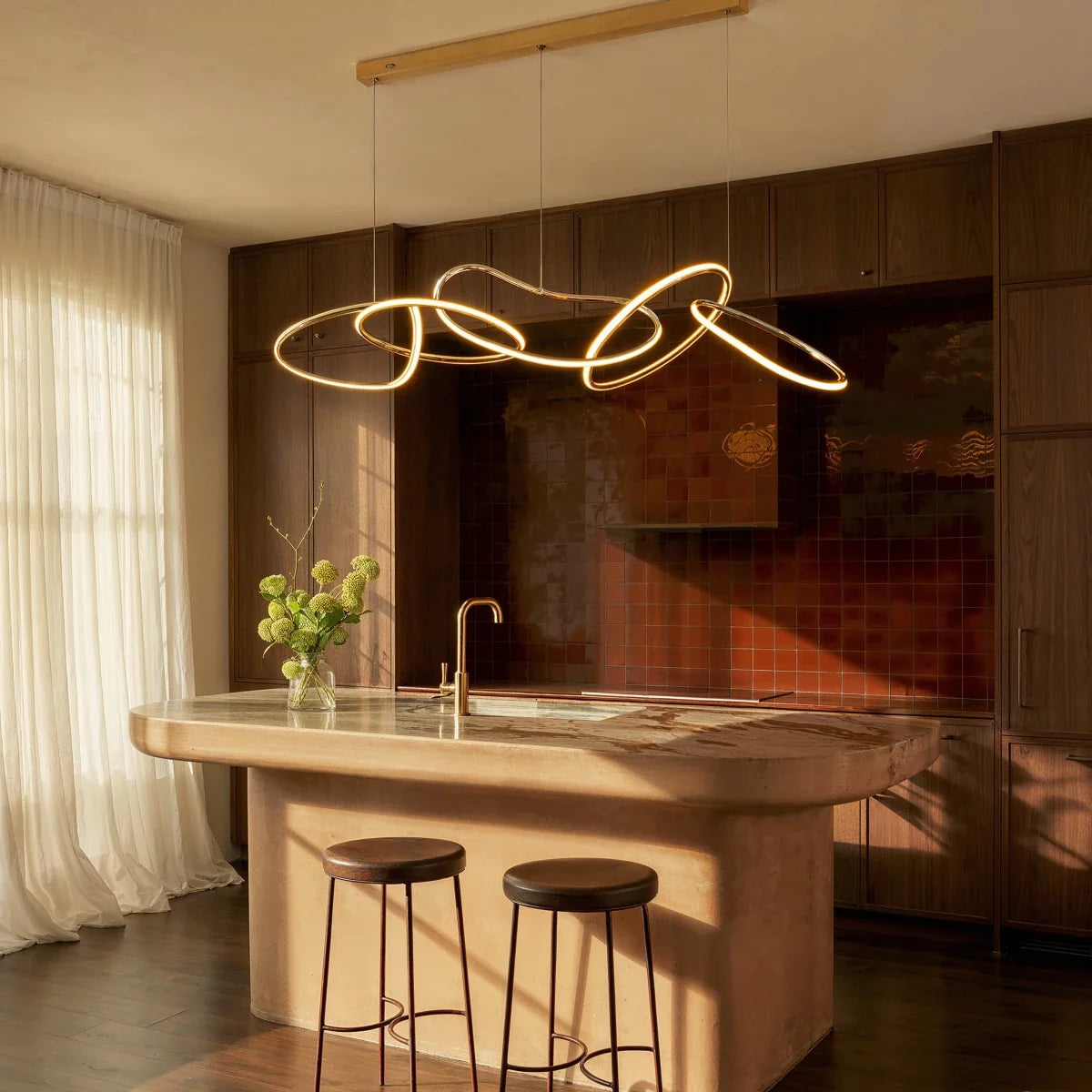 Clérachic chandelier hung over a stone kitchen island, its gold loops glowing warm above bar stools at sunset.