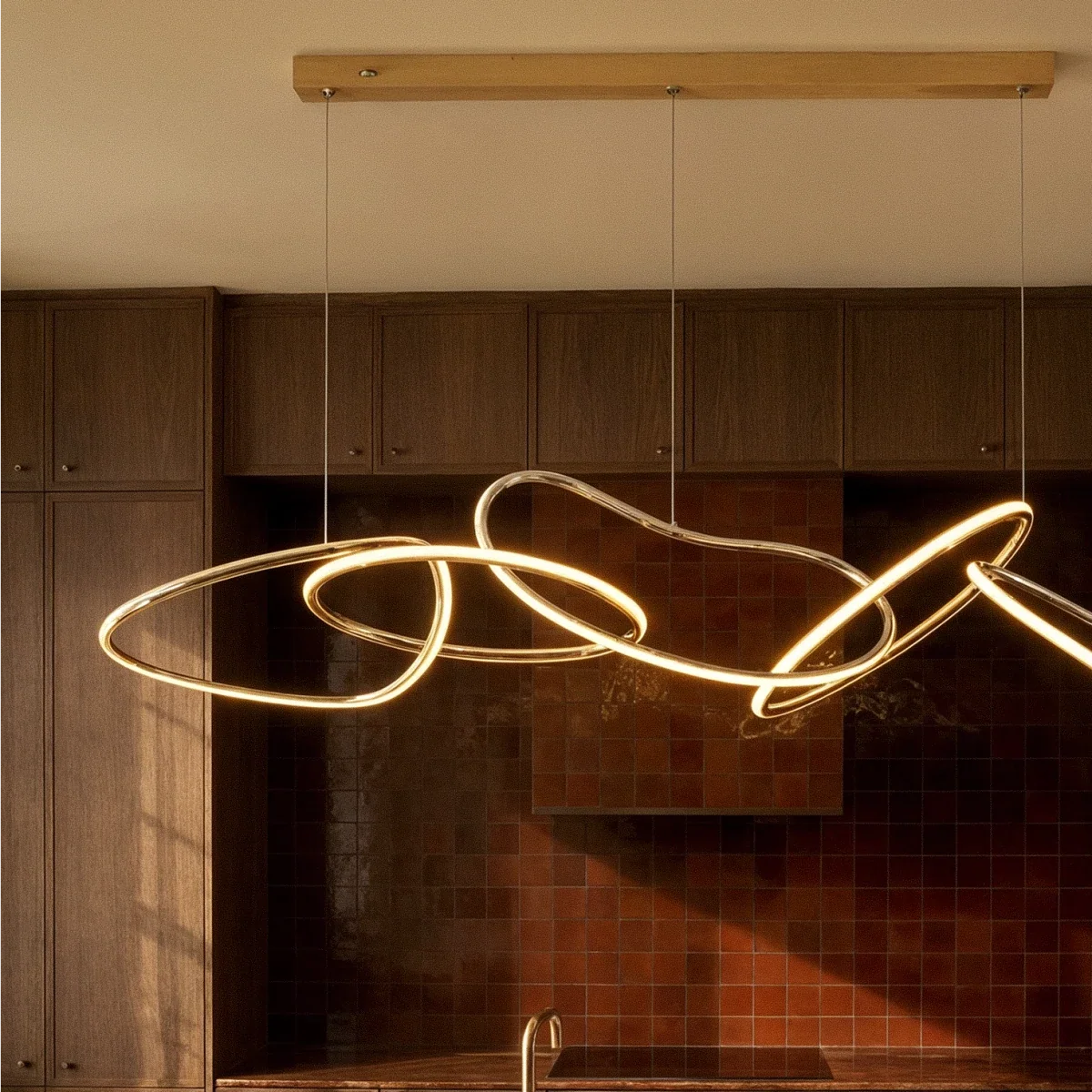 Clérachic chandelier centred above a kitchen island, its gold rings catching evening light against dark wood cabinets.