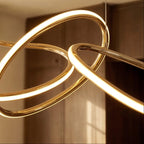 Close-up of the Clérachic chandelier's brushed gold tubing, showing where two illuminated rings cross and knot.