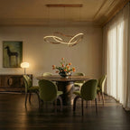 Clérachic chandelier centred over a round dining table, its rose gold loops glowing above green upholstered chairs.