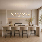 This Clérachic linear chandelier winds across a kitchen above a pale stone island with four tall bar stools.