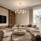 Above a round marble coffee table and a curved cream sofa, a Clérachic petal chandelier glows in a living room with a wall TV.