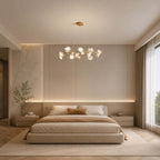 Clérachic round petal chandelier hung in a bedroom with a low upholstered bed, a marble wall panel and a strip of warm light.